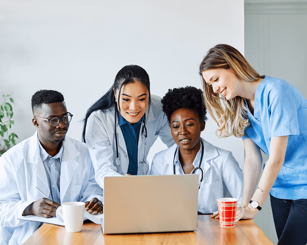 Four diverse healthcare professionals gathered around a laptop, engaged in discussion.